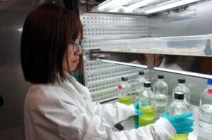 A woman in white lab coat working with bottles.