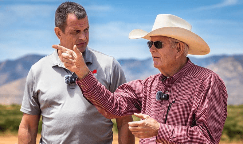 Two men outdoors, one explaining something to the other.