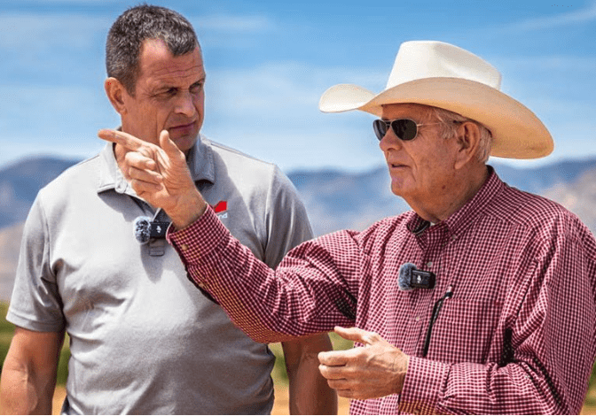 Two men outdoors, one explaining something to the other.